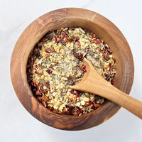 Wooden bowl with a wooden spoon containing a mix of dried herbs and spices on a white background