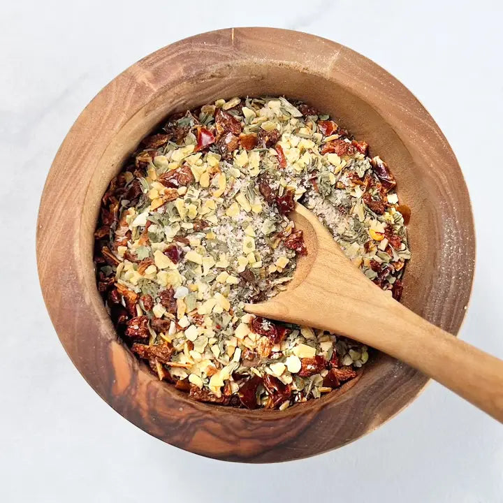 Wooden bowl with a wooden spoon containing a mix of dried herbs and spices on a white background