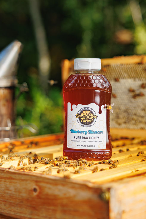 Bottle of honey with a beekeeper's tool and honeycomb in the background