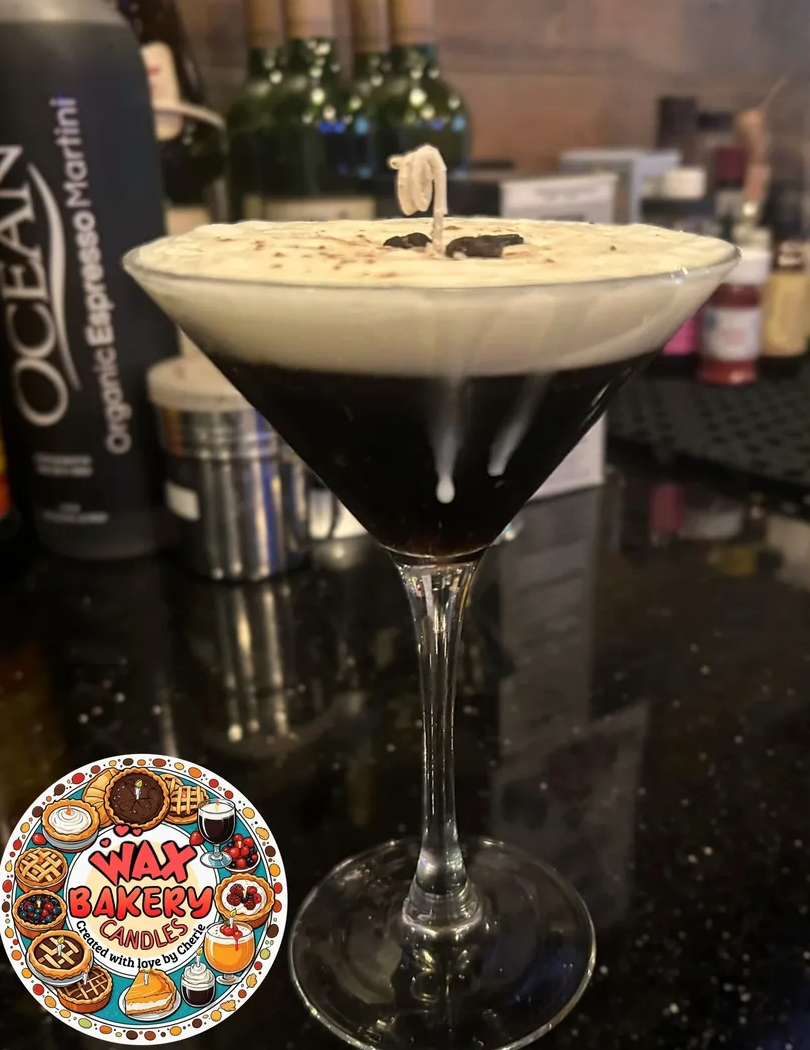 Dark cocktail in a martini glass with a lit candle on a bar counter, featuring Wax Bakery Candles logo.